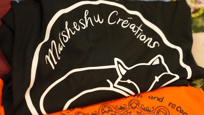 Un logo est apposé sur une pièce de tissus, il est écrit Matsheshu Créations au dessus d'un dessin représentant un renard. 