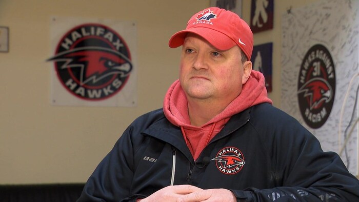 Un homme dans un aréna, coiffé d'une casquette rouge de Hockey Candaa et portant un blouson du club des Hawks.