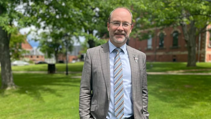 Un homme en complet chic et moderne, les deux mains dans les poches, debout sur une pelouse verdoyante.