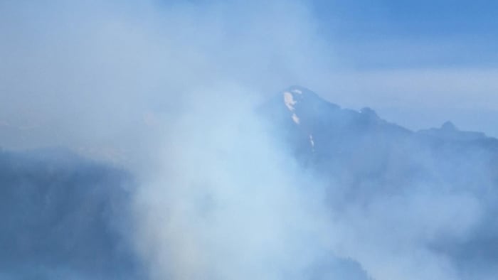 Fumée s'élevant de feux de forêt sur fond de montagne légèrement enneigée.