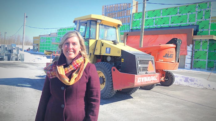 Mme Allaire prenant la pose devant un chantier de construction, en hiver.