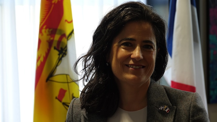 Une femme avec des cheveux mi-longs sourit à l'objectif devant des drapeaux.