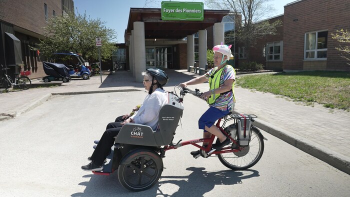 Maureen transporte deux résidents du Foyer des pionniers sur une bicyclette adapté.