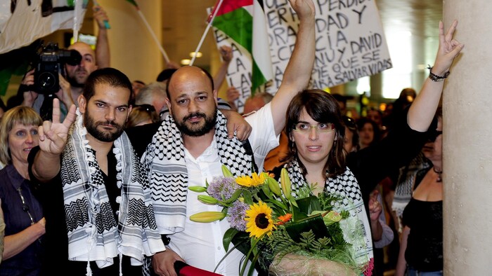 Deux hommes et une femme portant un keffieh autour du cou font le signe de la victoire.