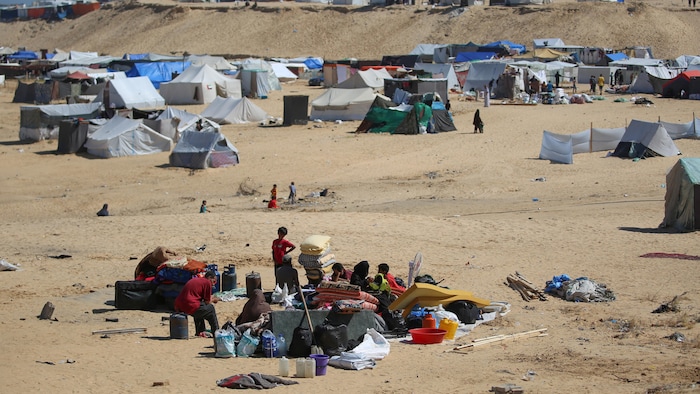 Des Palestiniens rassemblent matelas et sacs dans un secteur désertique où l'on voit des tentes.