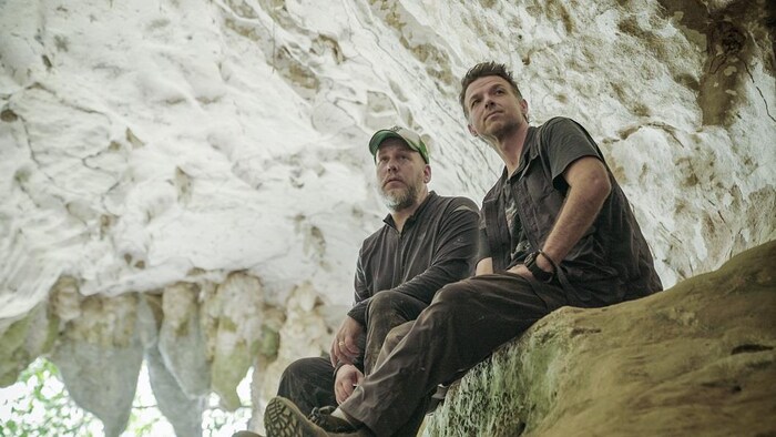 Deux hommes se tiennent sur un rocher dans une grotte.