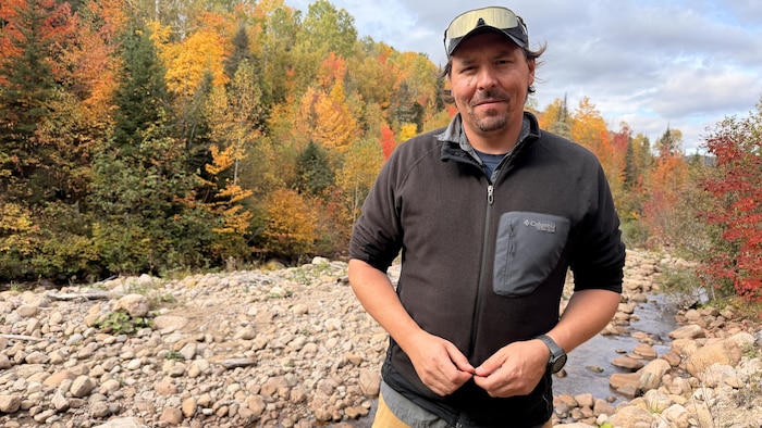 Un homme devant une rivière sourit à la caméra.