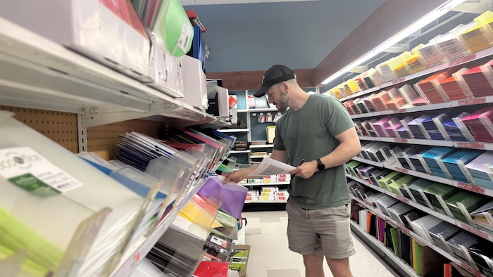 Maxime Clément sélectionne des fournitures scolaires dans une rangée de la Biblairie GGC.