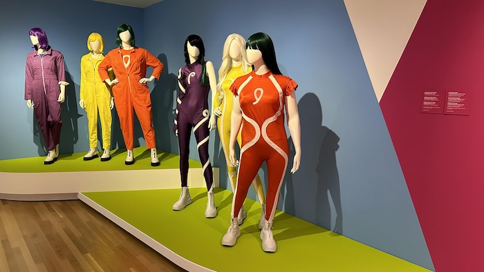 Six silhouettes de mannequins en plastique arborent des tenues colorées, s'apparentant à des habits d'astronautes.