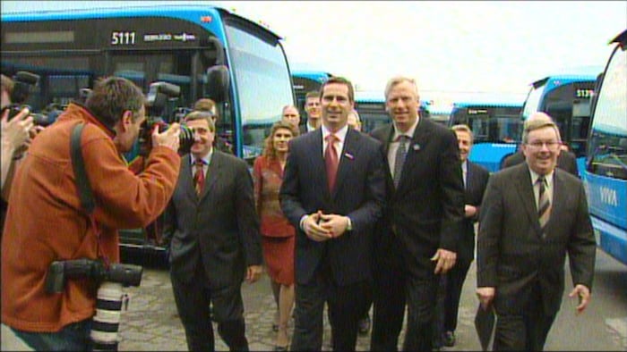 Dalton McGuinty et David Miller marchent côte à côte dans un terrain de stationnement rempli d’autobus.