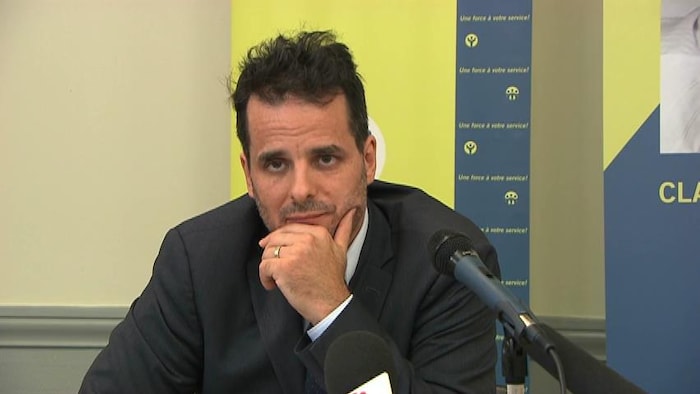Un homme devant des micros, assi à une table.