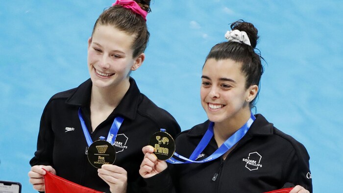 Les deux femmes, souriantes, montrent fièrement leur médaille et tiennent un drapeau canadien.
