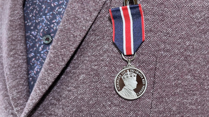 Une médaille sur un veston. Un portrait du roi Charles III et les mots « Charles III Dei Gratia Rex - Canada» y sont gravés.