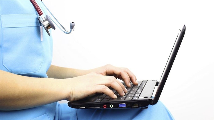 Un professionnel de la santé écrit sur un ordinateur portable placé sur ses genoux.