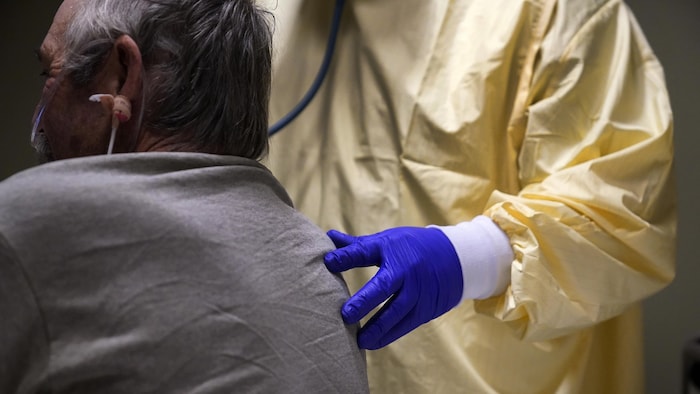 Un médecin met sa main gantée sur le dos d'un patient et place un stéthoscope sur sa poitrine.