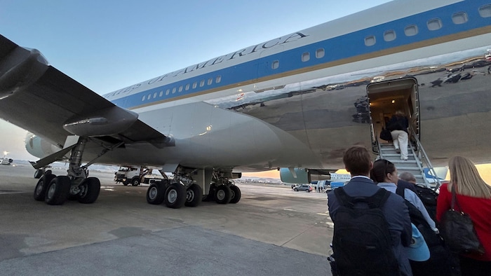 Quelques personnes debout sur le tarmac s'apprêtent à monter dans l'avion Air Force One par une porte à l'arrière d'une aile.