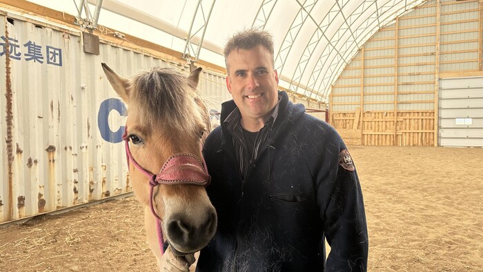 Martin Gendron sourit à la caméra en compagnie de son cheval, dans son écurie.