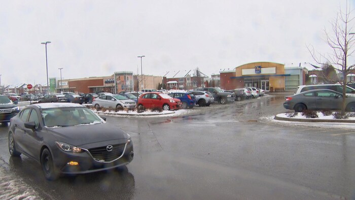 Plusieurs voitures dans un stationnement entouré de magasins. 