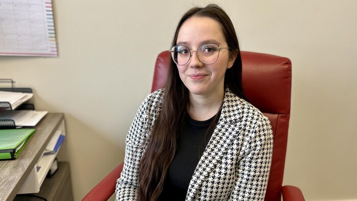 Une femme assise à un bureau, sourit à la caméra.