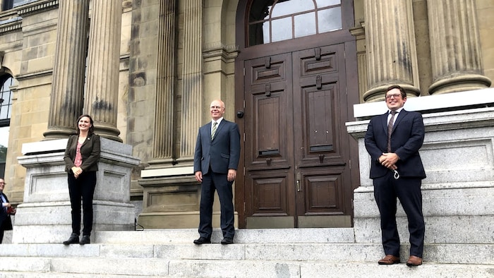 Trois personnes à l'extérieur sur les marches d'un édifice.