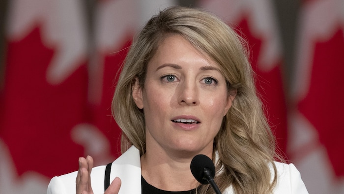 Mélanie Joly parle au micro devant des drapeaux du Canada.