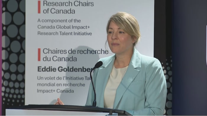 La ministre Mélanie Joly lors devant une affiche des Chaires de recherche du Canada Eddie Goldenberg