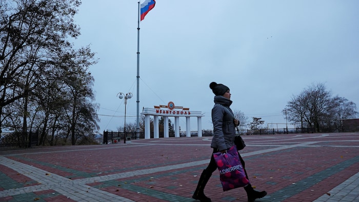 Une femme marche à l'extérieur dans la ville de Melitopol et un drapeau russe flotte derrière elle.