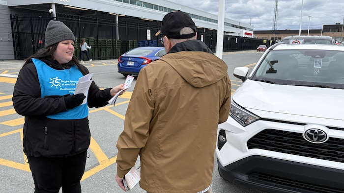Vanessa-Anne Paré distribue des papiers à une personne devant un stationnement pour personnes à mobilité réduite. 