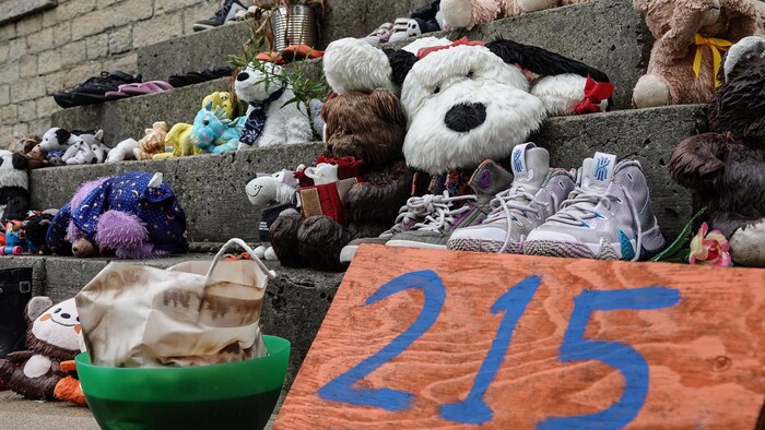 Des souliers et des jouets d'enfants sont disposés sur des marches et on peut lire le nombre 215 sur une affiche.