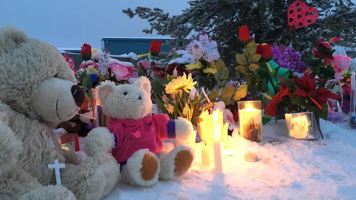 Des peluches et des bougies installés sur la neige, devant une école.