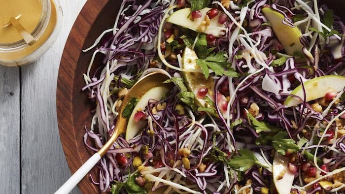 Photographie d'une salade dans un plat en bois avec une sauce sur le côté.