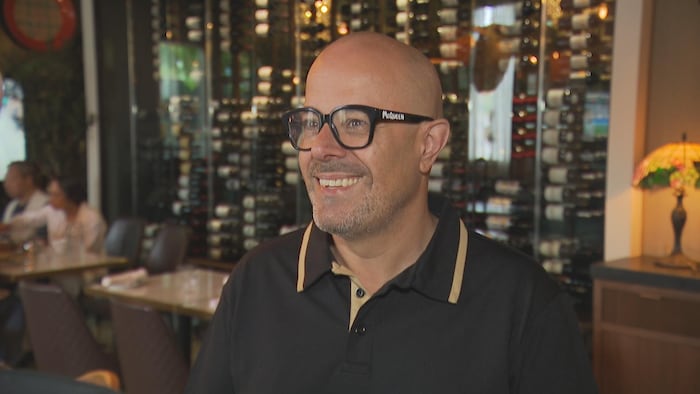 Un homme portant des lunettes pose devant la cave à vin de son restaurant portugais de Toronto.