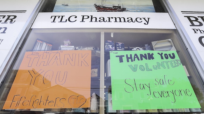 Des écriteaux sur du papier construction vert et orange dans les fenêtres d'une pharmacie. On y a écrit des messages de remerciements pour les pompiers.