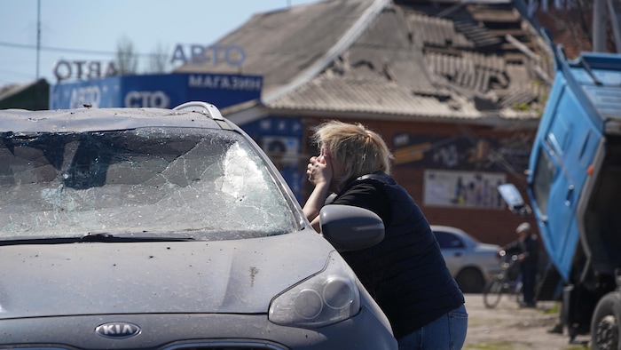 Une femme en pleurs devant une auto endommagée