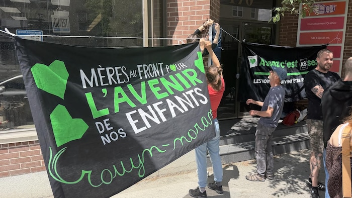 Des gens posent une banderole devant un bureau de député en vue d'une manifestation.