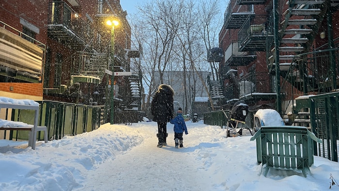Une mère tient la main de son fils devant des logements.