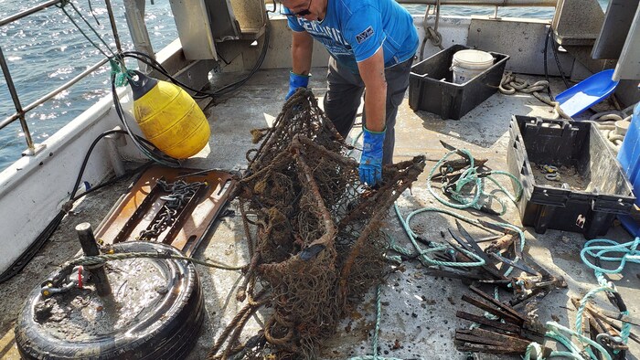 Un vieux casier de pêche est manipulé à bord d'un bateau.