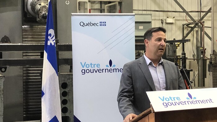 Éric Martin s'adresse au public. Il est dans les installations de sa compagnie. Derrière lui, une pancarte du gouvernement du Québec.