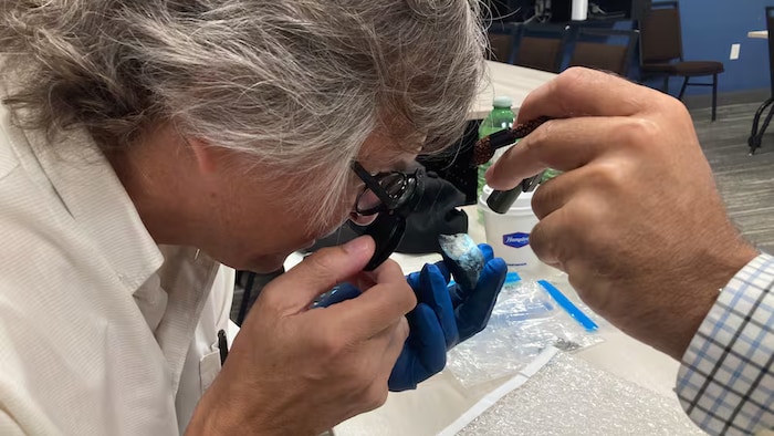 Phil McCausland examine une pierre en regardant dans une loupe.