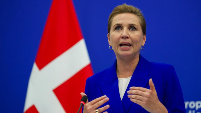 Mette Frederiksen parle pendant une conférence de presse devant un drapeau du Danemark.