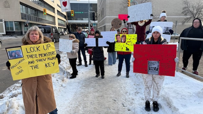 Des manifestants venus au procès d'Irene Lima et Chad Kabecz posent avec leurs pancartes.