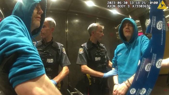 L'accusé sous escorte policière dans un ascenseur.