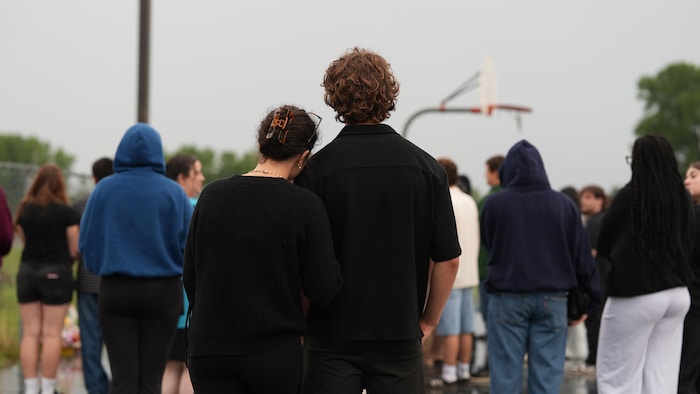 Des jeunes, debout sous la pluie, sur un terrain de basket.