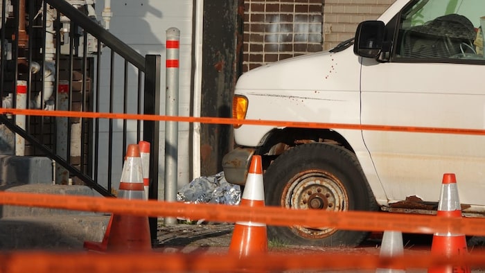 Une scène de crime est délimitée. On voit derrière le ruban orange une couverture en aluminium qui recouvre le corps d'une personne assassinée.