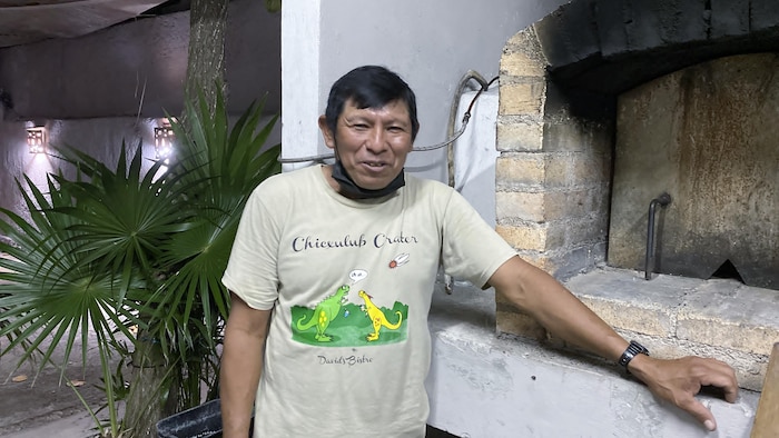 He smiles in front of a brick oven. 