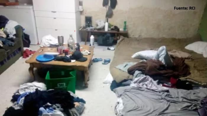 Une salle malpropre avec un matelas et des vêtements éparpillés.