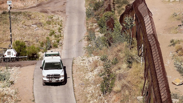 On voit une voiture des agents frontaliers américains circuler tout près de la palissade qui sépare les États-Unis du Mexique. 