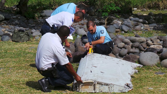 Des gendarmes et des policiers français inspectent un gros morceau de débris d'avion trouvé sur la plage de Saint-André, sur l'île française de La Réunion, dans l'océan Indien, le 29 juillet 2015.
