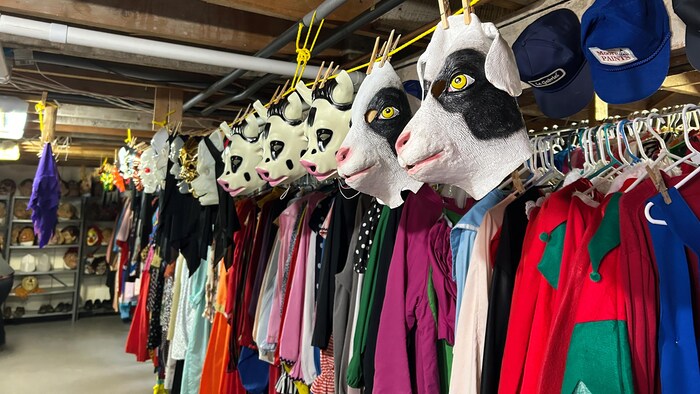 Des masques de têtes de chèvre et de cochon sont suspendus avec des épingles à linge au-dessus de rangées de vêtements.