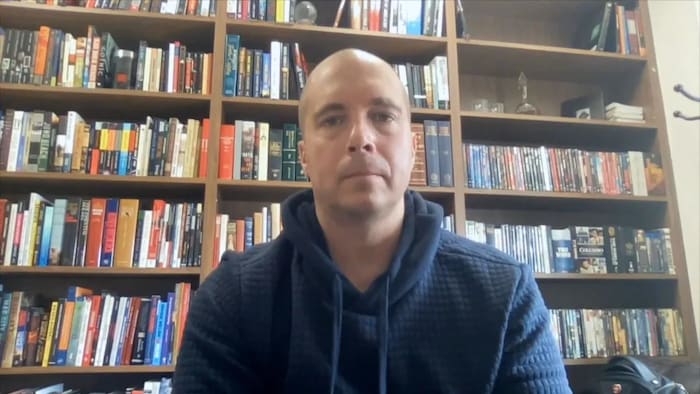 Michael Arntfield est assis devant des étagères remplies de livres.